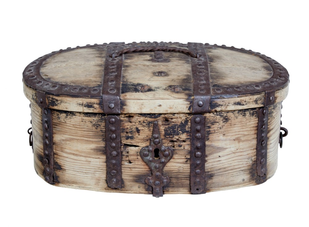 An oval Swedish pine box featuring decorative wrought iron straps, stud detailing, a central keyhole escutcheon, and a top twisted iron handle.