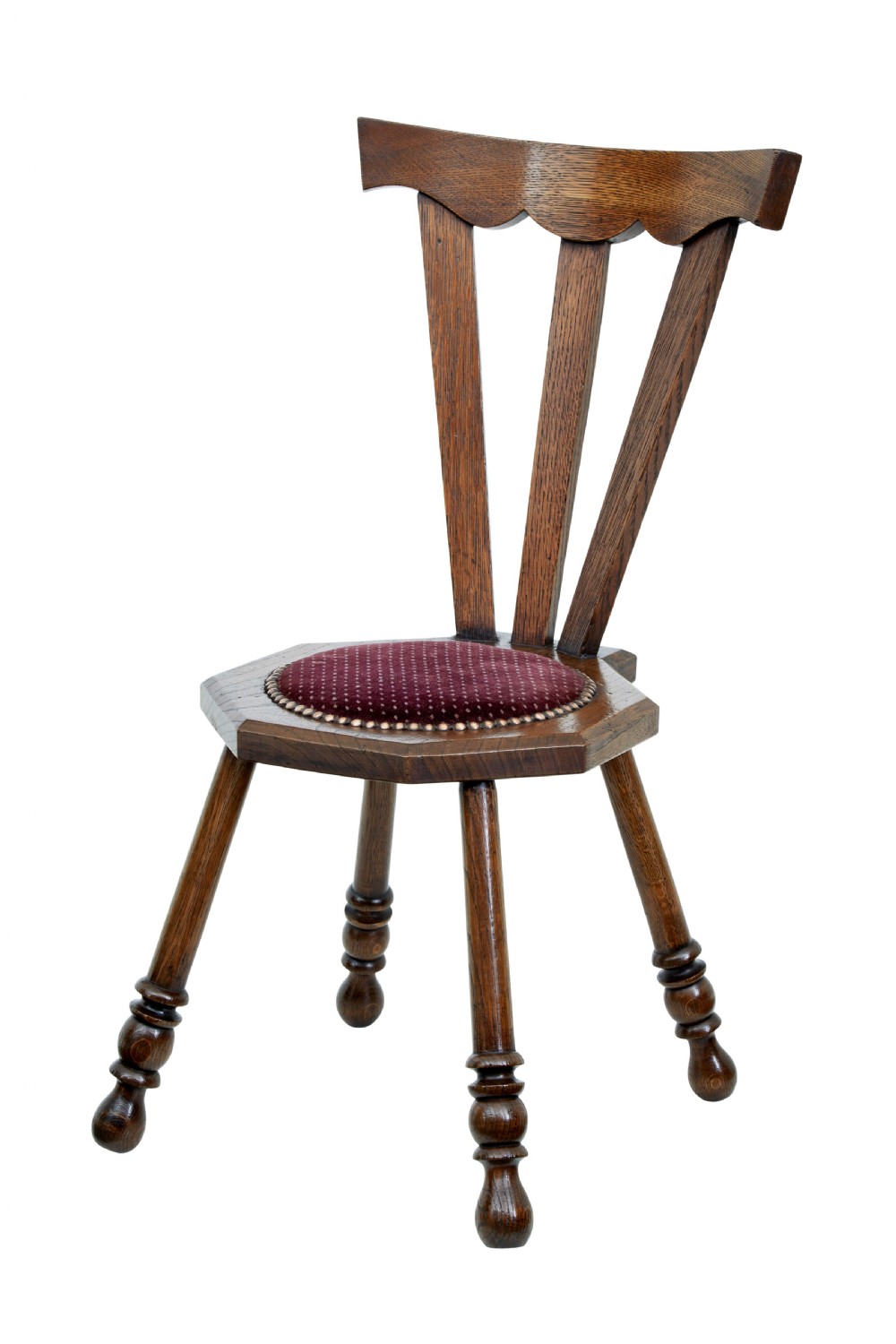 An early 20th-century Arts and Crafts oak childs chair featuring a sculpted top rail, three back splats, a hexagonal seat with red velvet upholstery, and turned splayed legs.