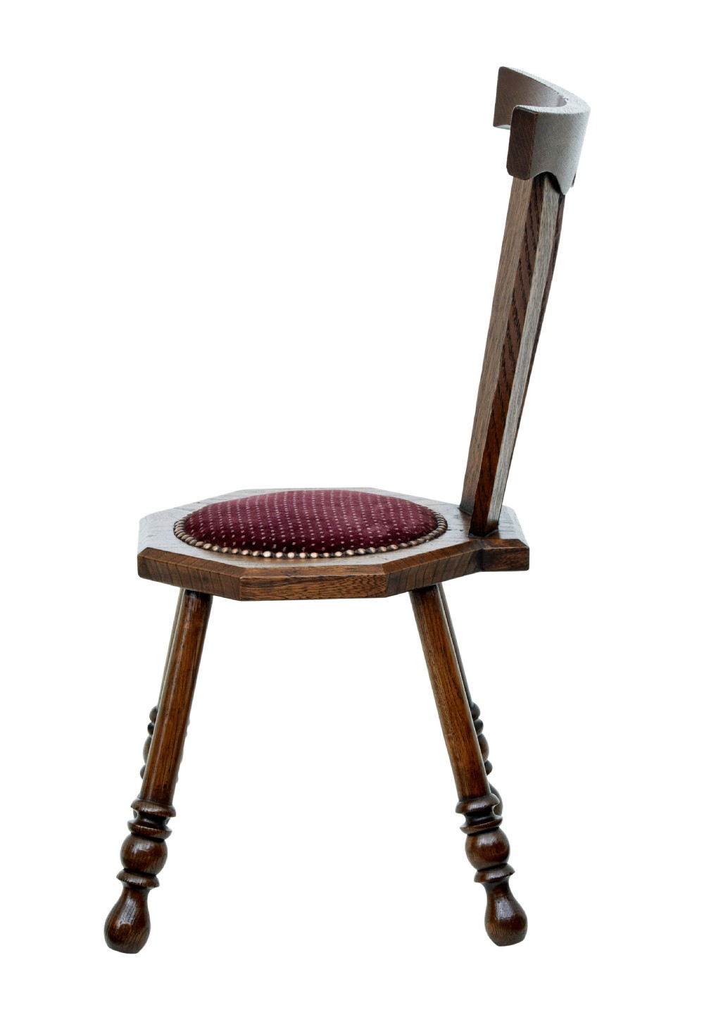 An early 20th-century Arts and Crafts oak childs chair featuring a sculpted top rail, three back splats, a hexagonal seat with red velvet upholstery, and turned splayed legs. View III