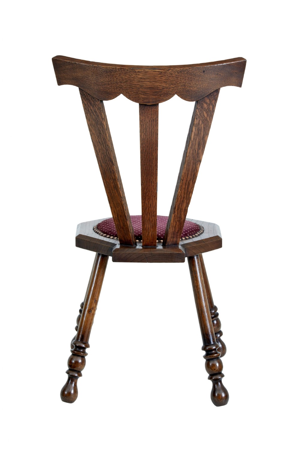 An early 20th-century Arts and Crafts oak childs chair featuring a sculpted top rail, three back splats, a hexagonal seat with red velvet upholstery, and turned splayed legs. View IV