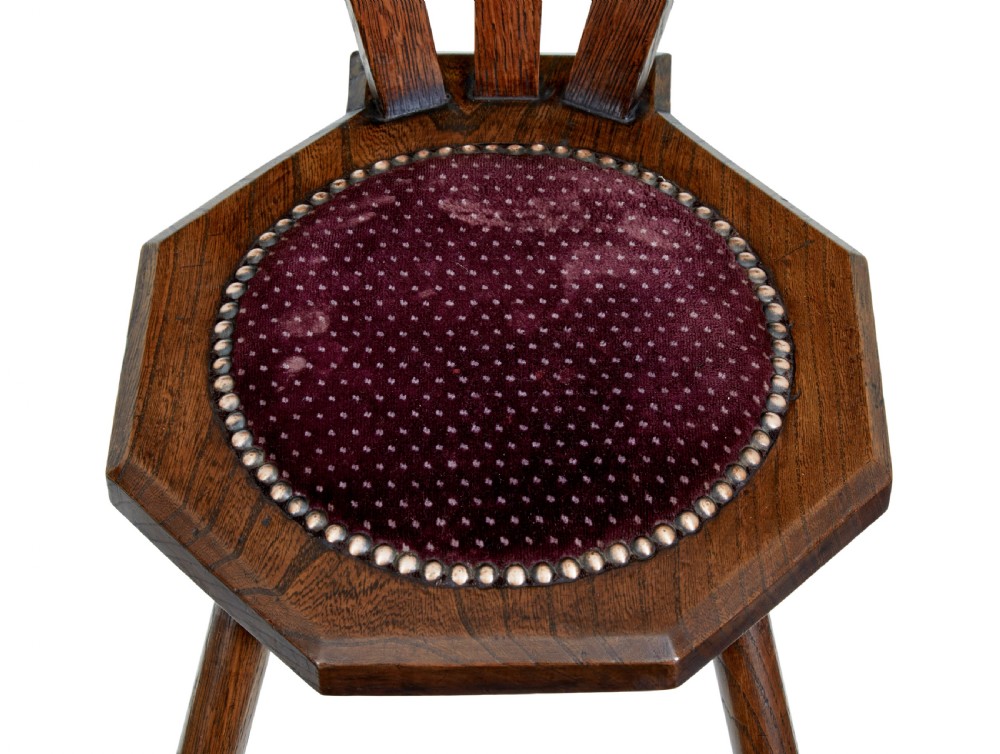 An early 20th-century Arts and Crafts oak childs chair featuring a sculpted top rail, three back splats, a hexagonal seat with red velvet upholstery, and turned splayed legs. View V