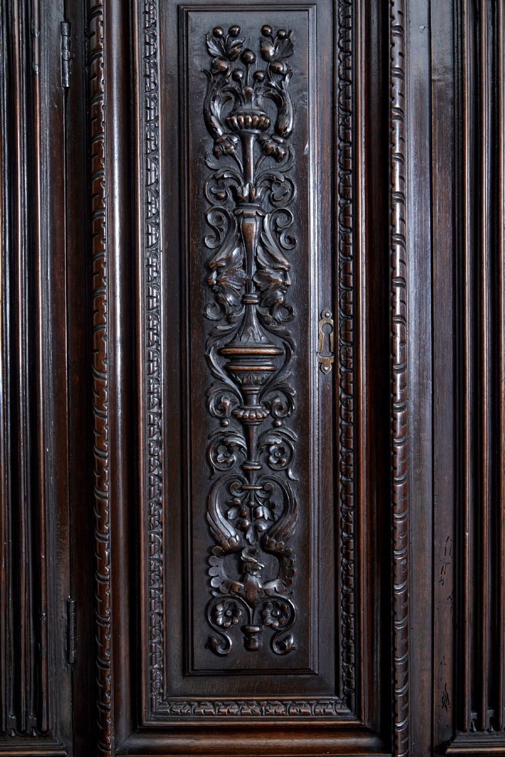 A two-section mid-19th century dark walnut cabinet featuring detailed relief carvings on the panelled doors, fluted columns, and flattened bun feet. View VI