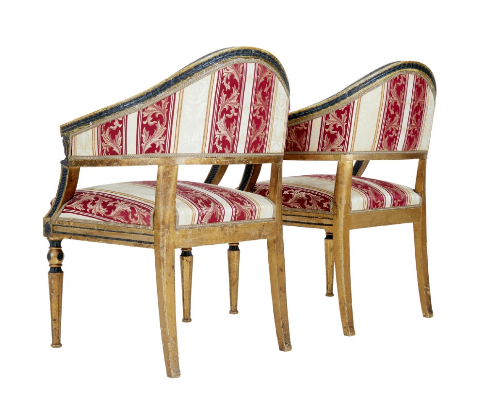 A pair of 19th-century Swedish giltwood armchairs featuring curved backs, black carved terminals with female heads, and red and cream striped fabric upholstery. View II