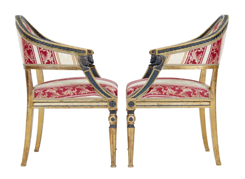 A pair of 19th-century Swedish giltwood armchairs featuring curved backs, black carved terminals with female heads, and red and cream striped fabric upholstery. View V