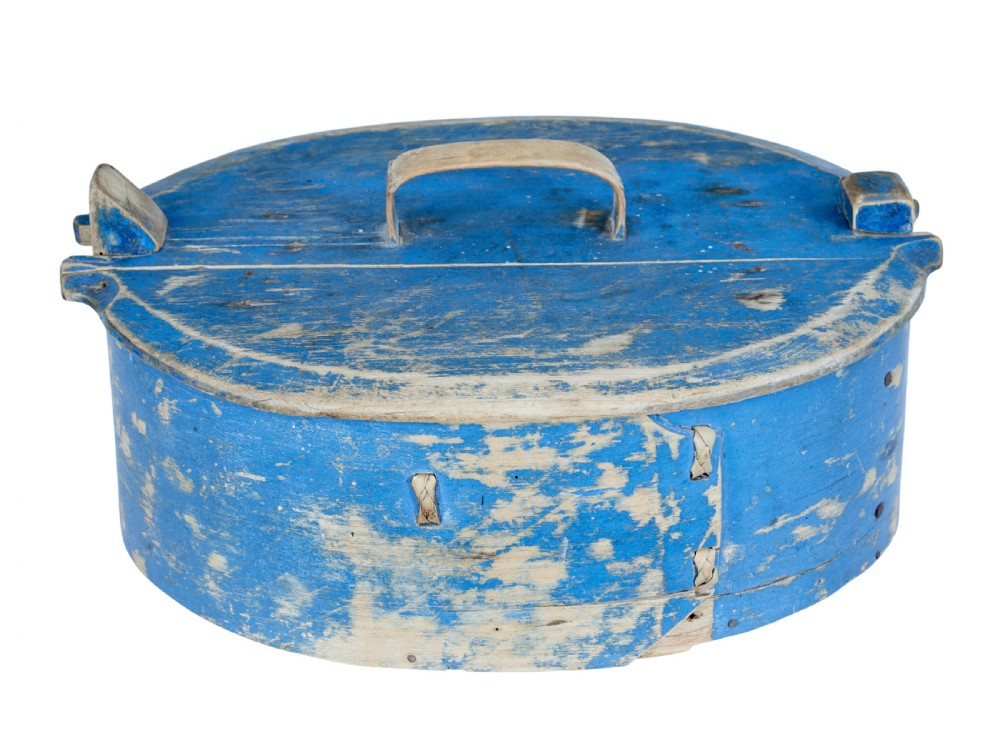 A 19th-century oval wooden tine box featuring distressed blue paint, vertical end pegs, a bentwood top handle, and root lacing.