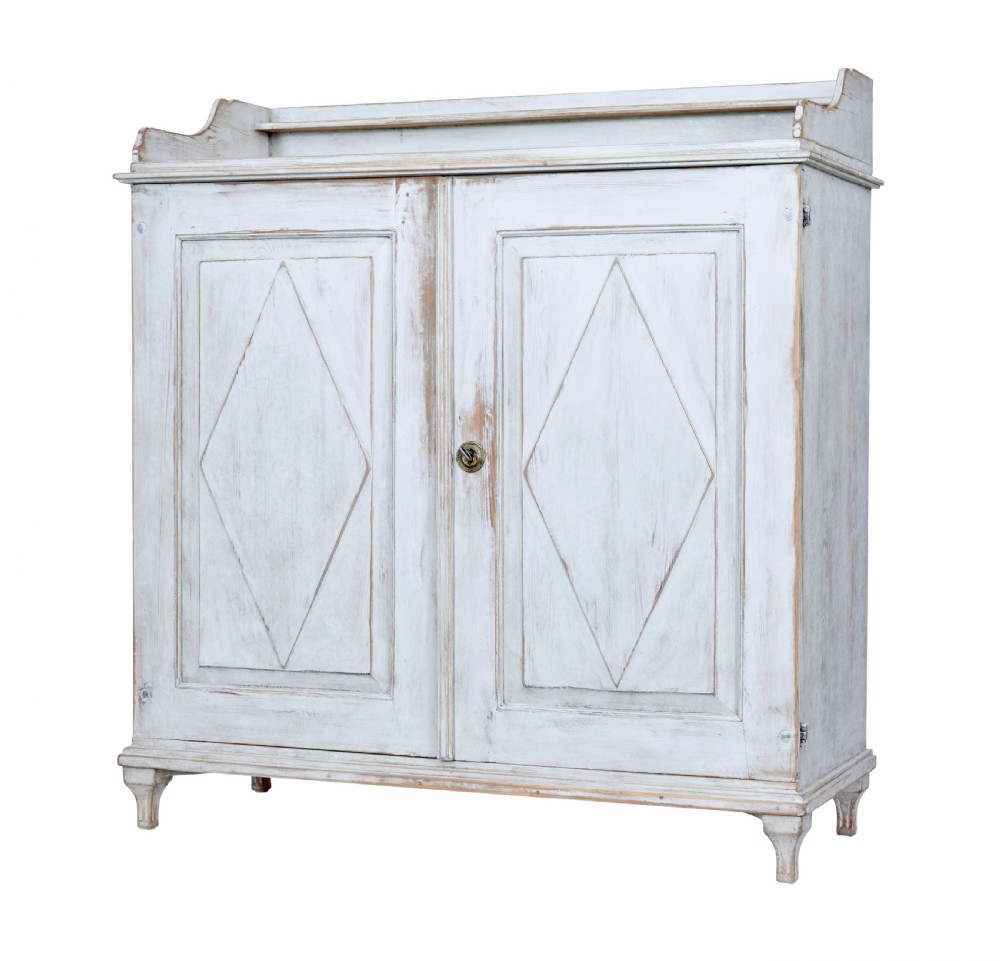 A 19th-century Swedish pine cupboard featuring distressed off-white painted finishes, double doors carved with diamond motifs, tapered short legs, and a low gallery top.