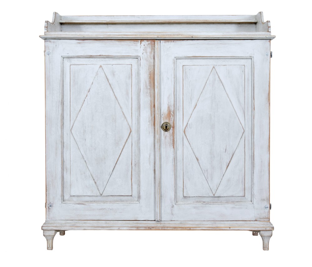 A 19th-century Swedish pine cupboard featuring distressed off-white painted finishes, double doors carved with diamond motifs, tapered short legs, and a low gallery top. View II