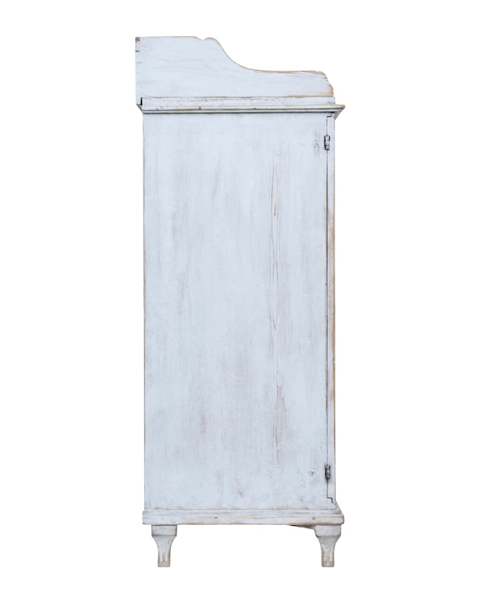 A 19th-century Swedish pine cupboard featuring distressed off-white painted finishes, double doors carved with diamond motifs, tapered short legs, and a low gallery top. View VI