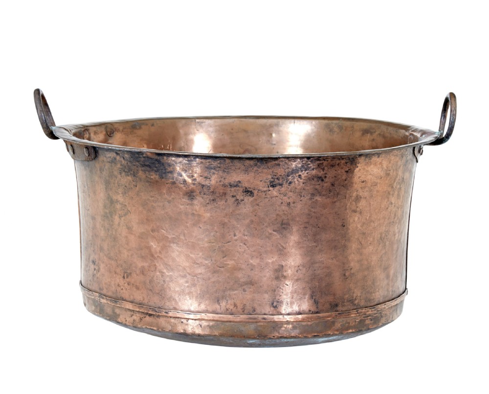 A large 19th-century hammered copper cooking vessel featuring a rounded base, riveted seams, and two wrought iron loop handles.