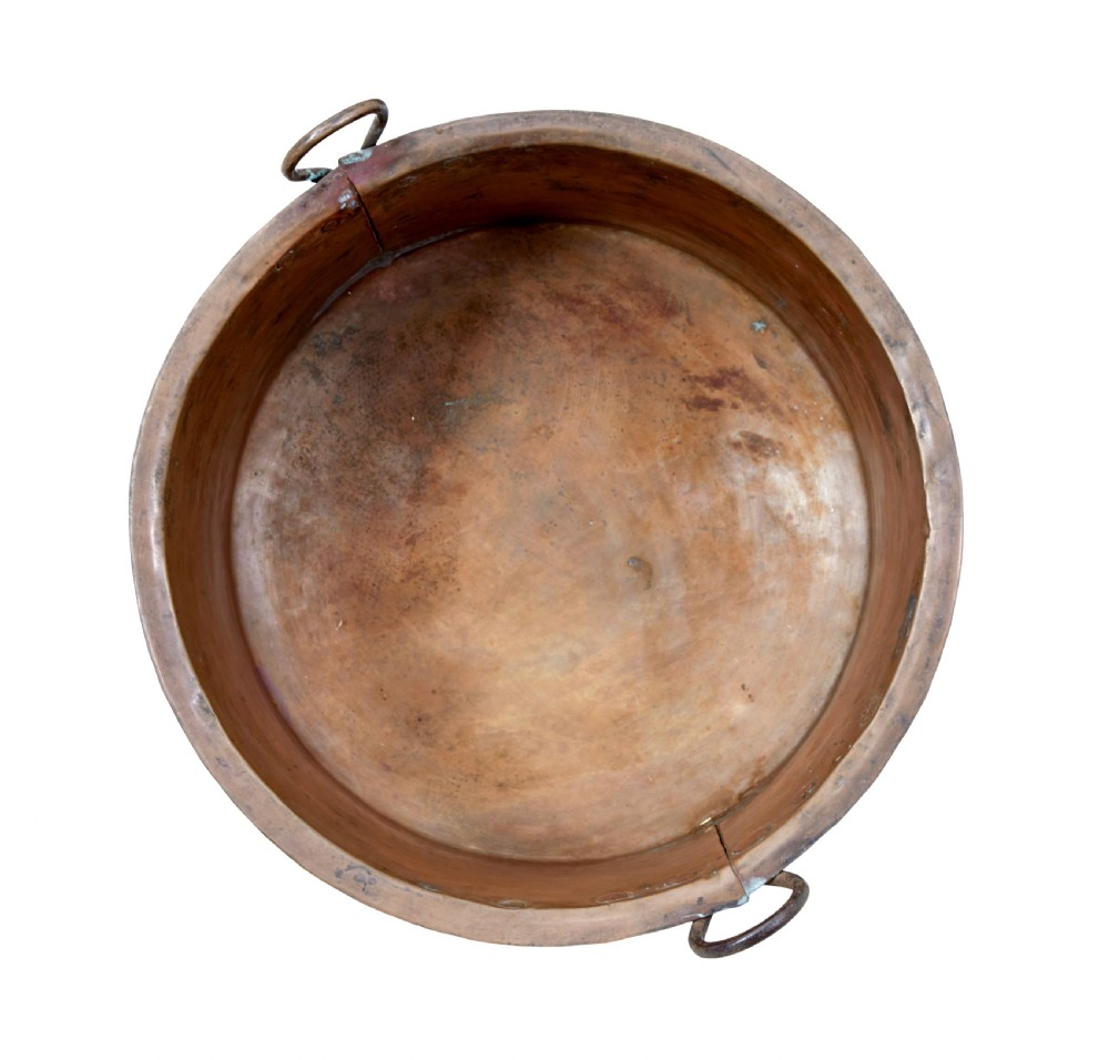 A large 19th-century hammered copper cooking vessel featuring a rounded base, riveted seams, and two wrought iron loop handles. View V