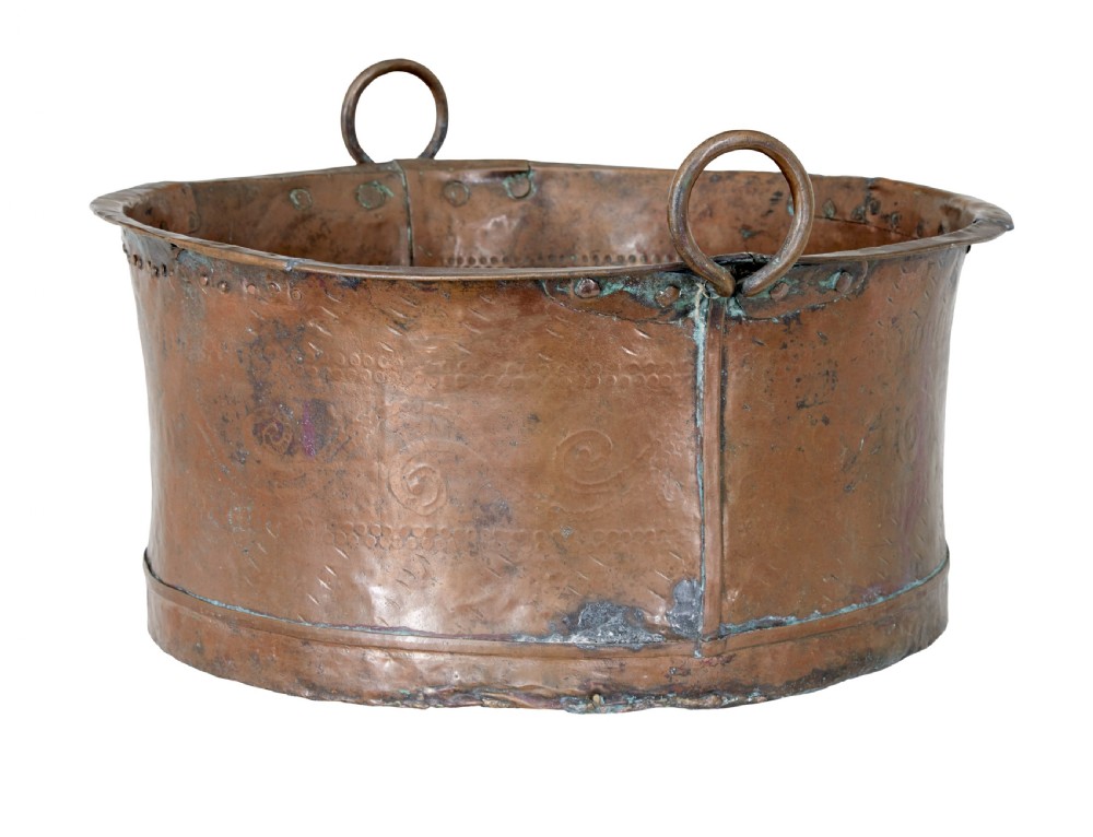 A large 19th-century copper pot with embossed spiral patterns, riveted side seams, a wide flared rim, and two round metal ring handles.