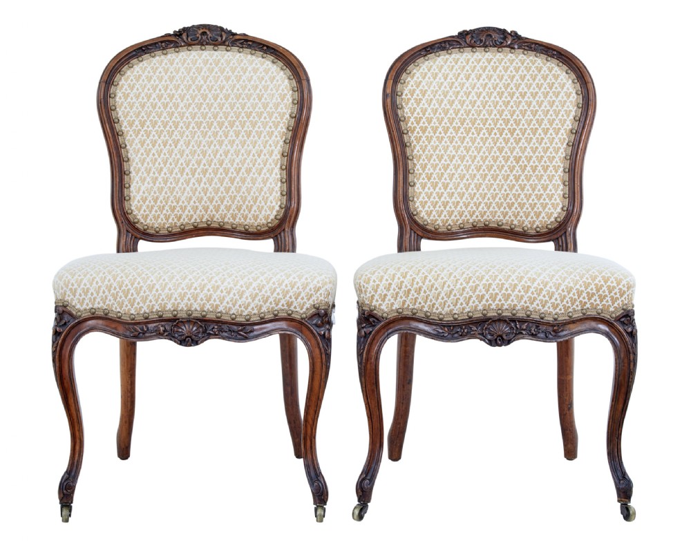A pair of 19th-century carved walnut side chairs with patterned beige upholstery, cabriole legs, and brass castors.