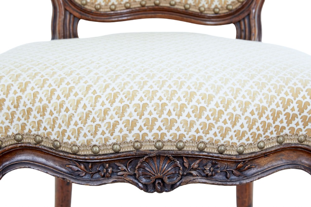 A pair of 19th-century carved walnut side chairs with patterned beige upholstery, cabriole legs, and brass castors. View V