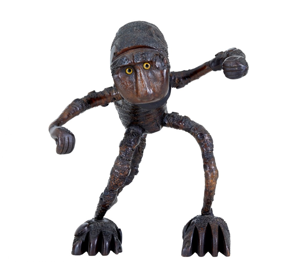A dark brown hand-carved mango wood novelty figure with inset yellow glass eyes and long textured limbs.