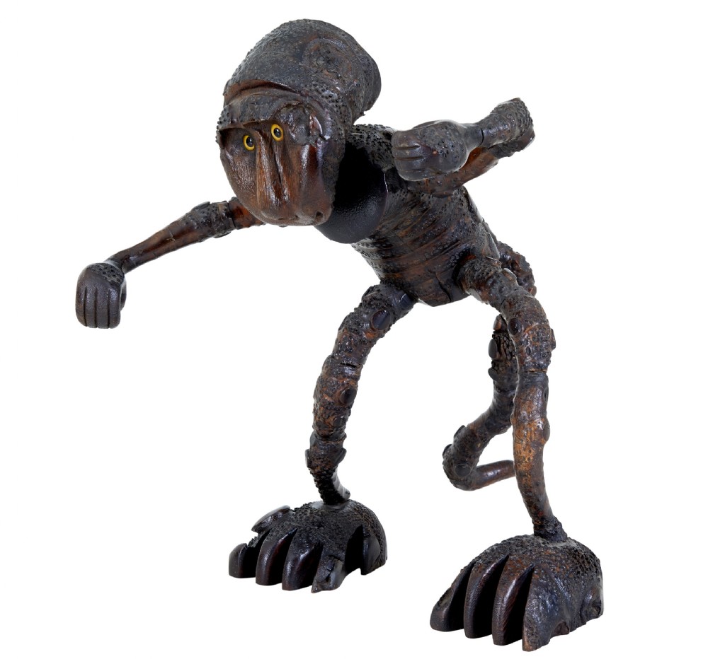 A dark brown hand-carved mango wood novelty figure with inset yellow glass eyes and long textured limbs. View II