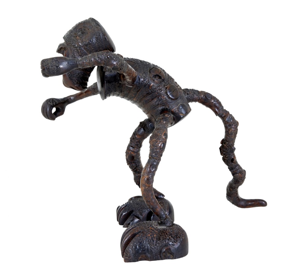 A dark brown hand-carved mango wood novelty figure with inset yellow glass eyes and long textured limbs. View III