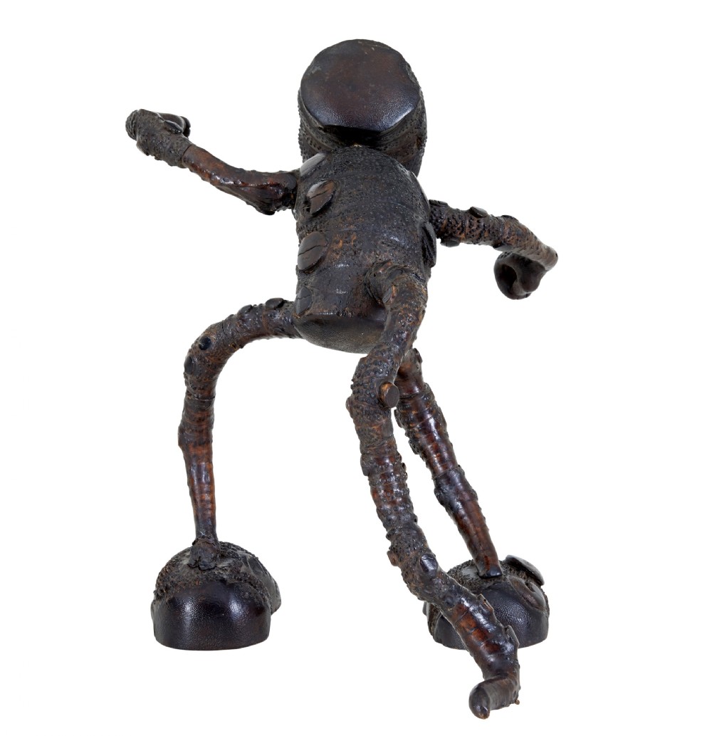 A dark brown hand-carved mango wood novelty figure with inset yellow glass eyes and long textured limbs. View IV