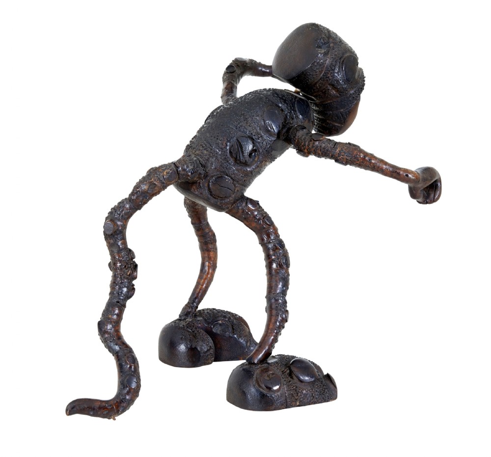 A dark brown hand-carved mango wood novelty figure with inset yellow glass eyes and long textured limbs. View V