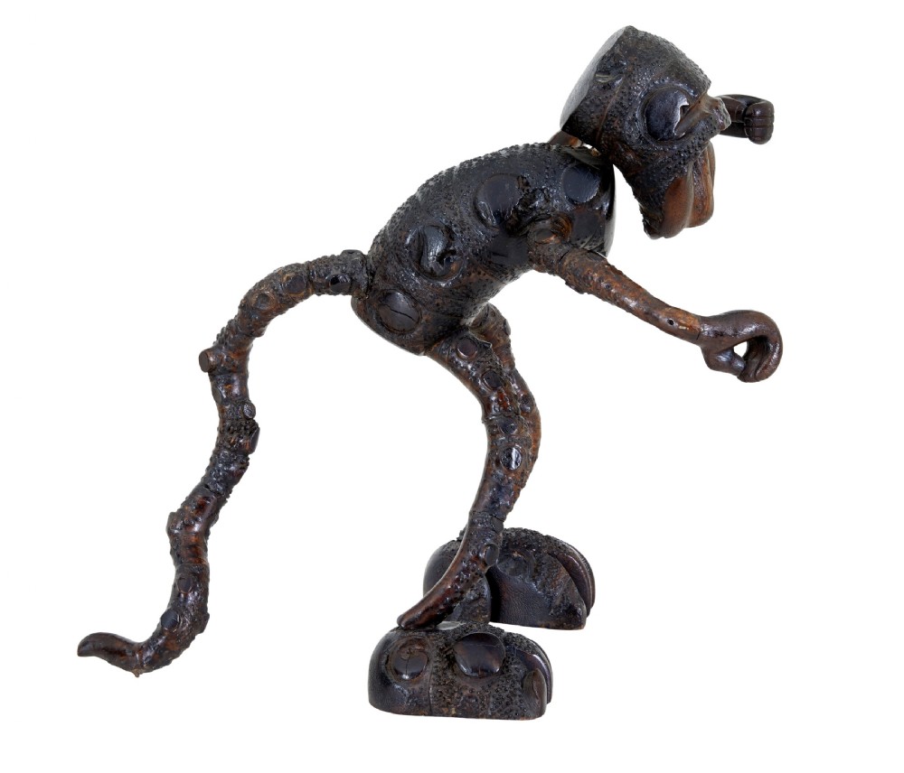 A dark brown hand-carved mango wood novelty figure with inset yellow glass eyes and long textured limbs. View VI