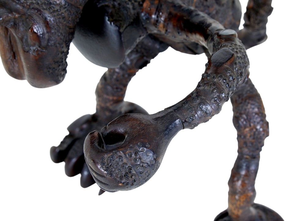 A dark brown hand-carved mango wood novelty figure with inset yellow glass eyes and long textured limbs. View VIII