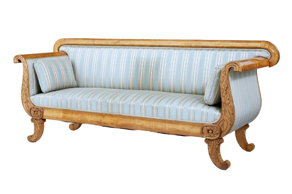 A 19th-century Swedish carved birch sofa featuring scrolled arms, floral rosettes, swept feet, and light blue and white striped upholstery.