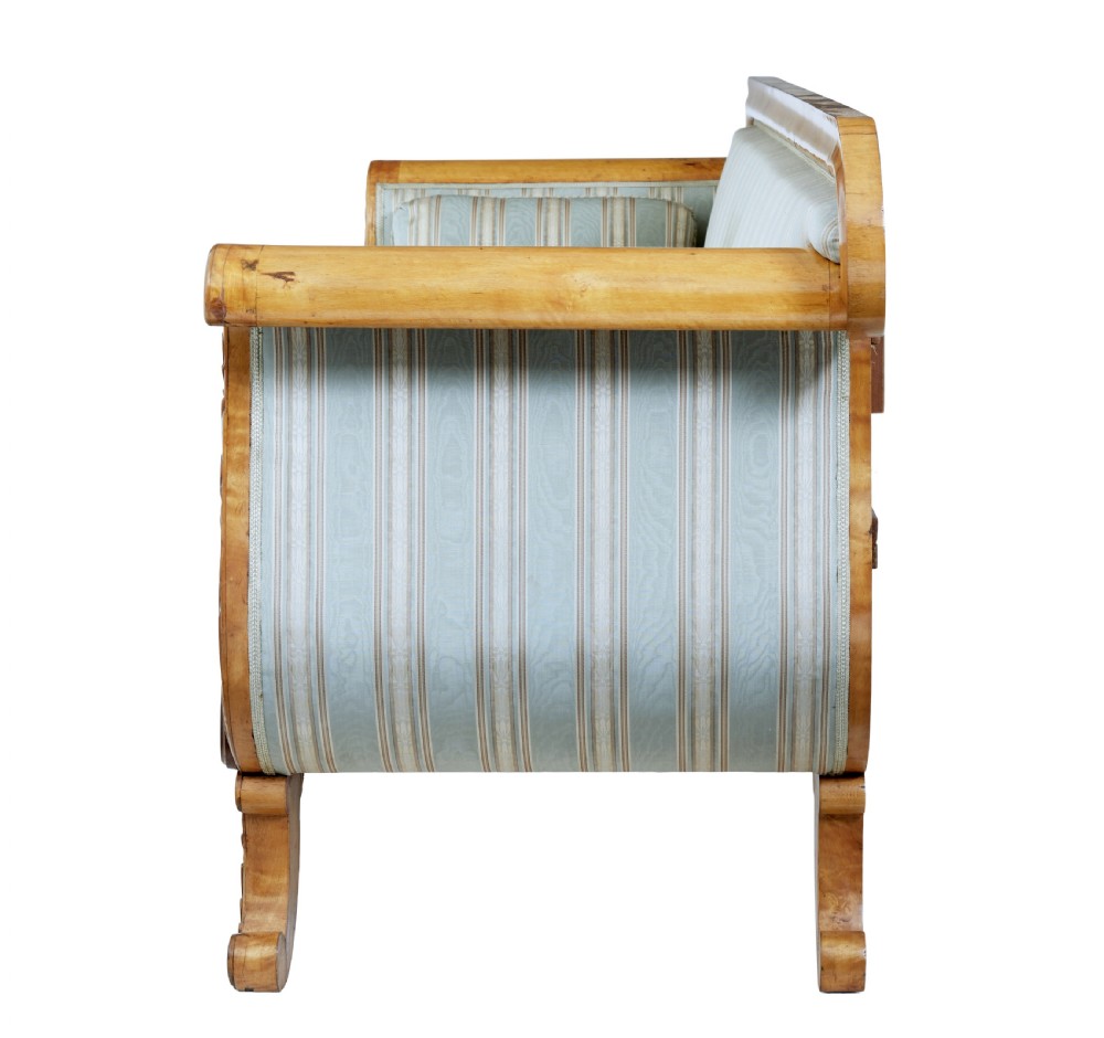 A 19th-century Swedish carved birch sofa featuring scrolled arms, floral rosettes, swept feet, and light blue and white striped upholstery. View V