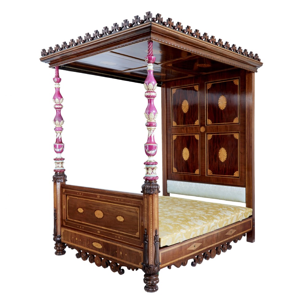 A nineteenth-century mahogany four-poster bed frame featuring carved posts with pink porcelain sections, marquetry panelling, and an ornate trefoil canopy trim.