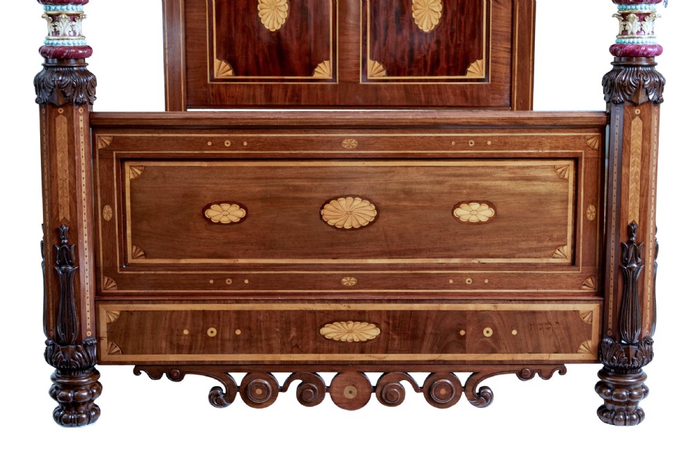 A nineteenth-century mahogany four-poster bed frame featuring carved posts with pink porcelain sections, marquetry panelling, and an ornate trefoil canopy trim. View VI