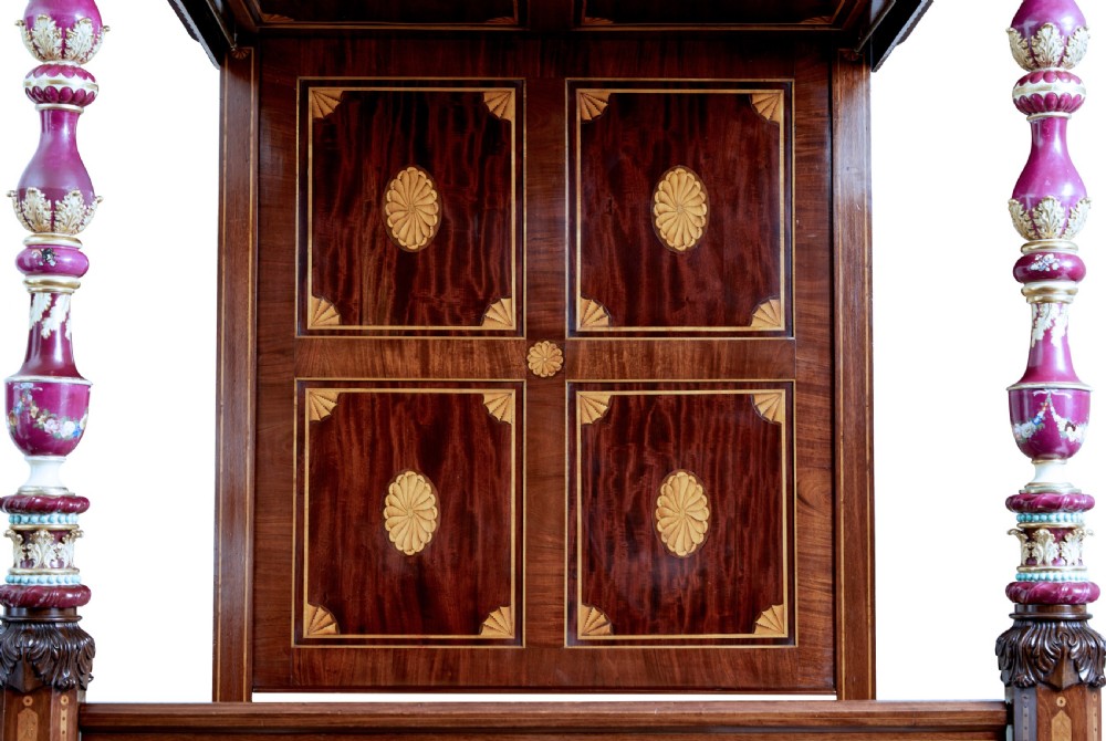 A nineteenth-century mahogany four-poster bed frame featuring carved posts with pink porcelain sections, marquetry panelling, and an ornate trefoil canopy trim. View VII