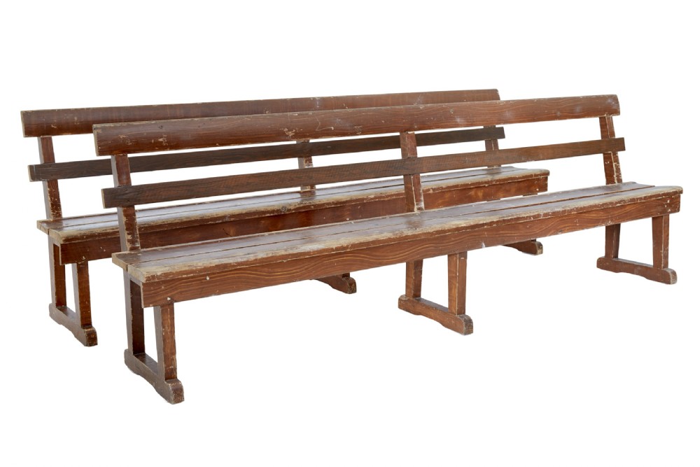 A pair of long, rustic pine benches with slatted backrests, trestle-style legs, and a distressed reddish-brown painted finish.