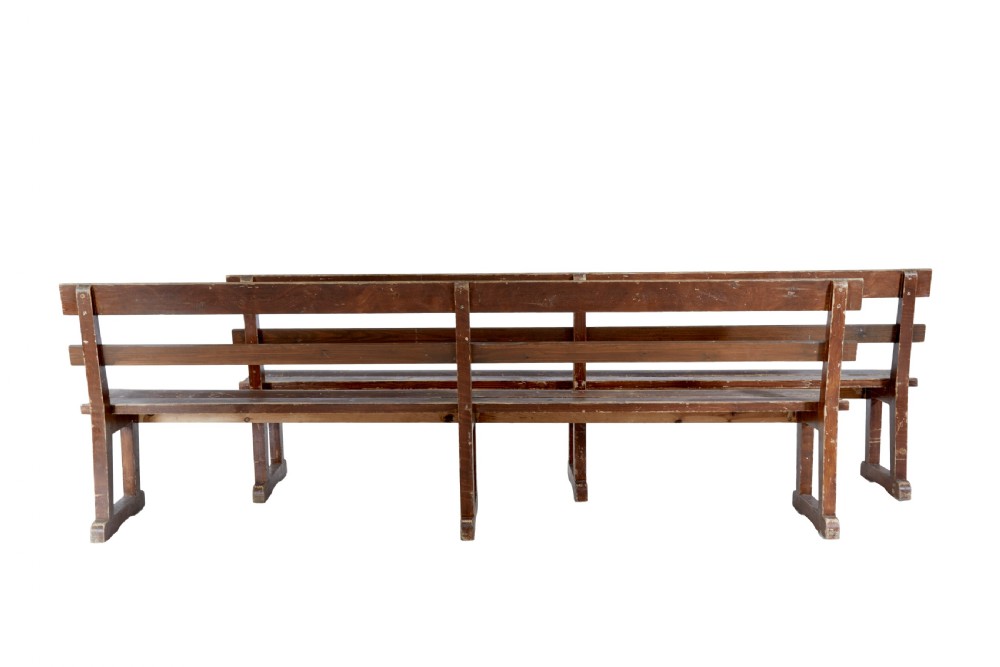 A pair of long, rustic pine benches with slatted backrests, trestle-style legs, and a distressed reddish-brown painted finish. View IV