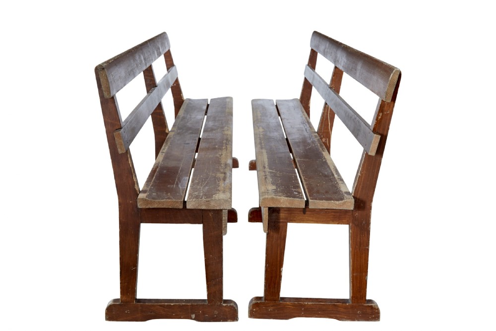 A pair of long, rustic pine benches with slatted backrests, trestle-style legs, and a distressed reddish-brown painted finish. View V