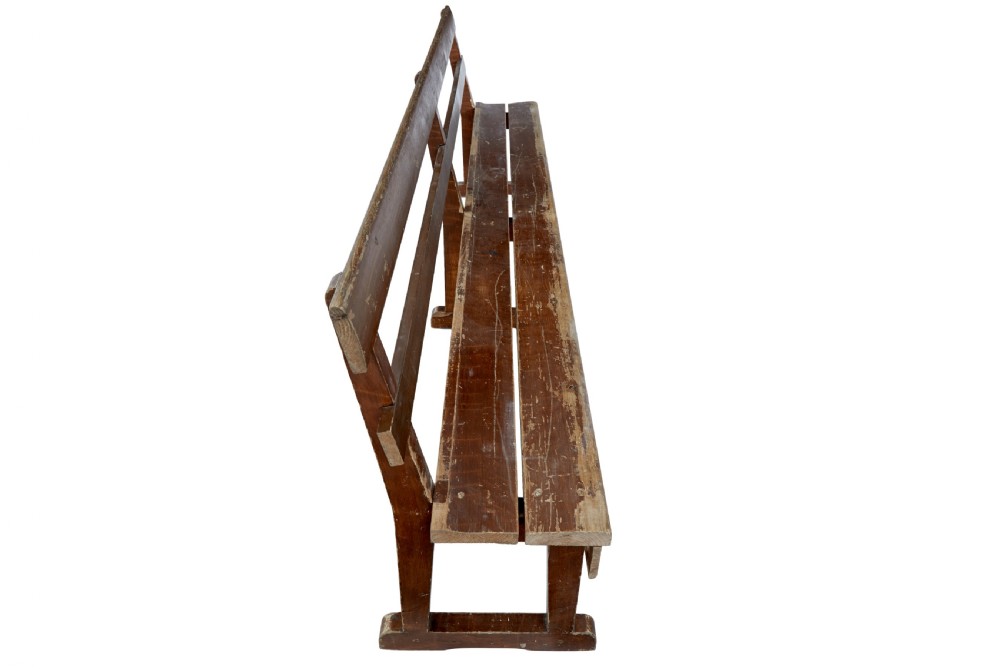 A pair of long, rustic pine benches with slatted backrests, trestle-style legs, and a distressed reddish-brown painted finish. View VI