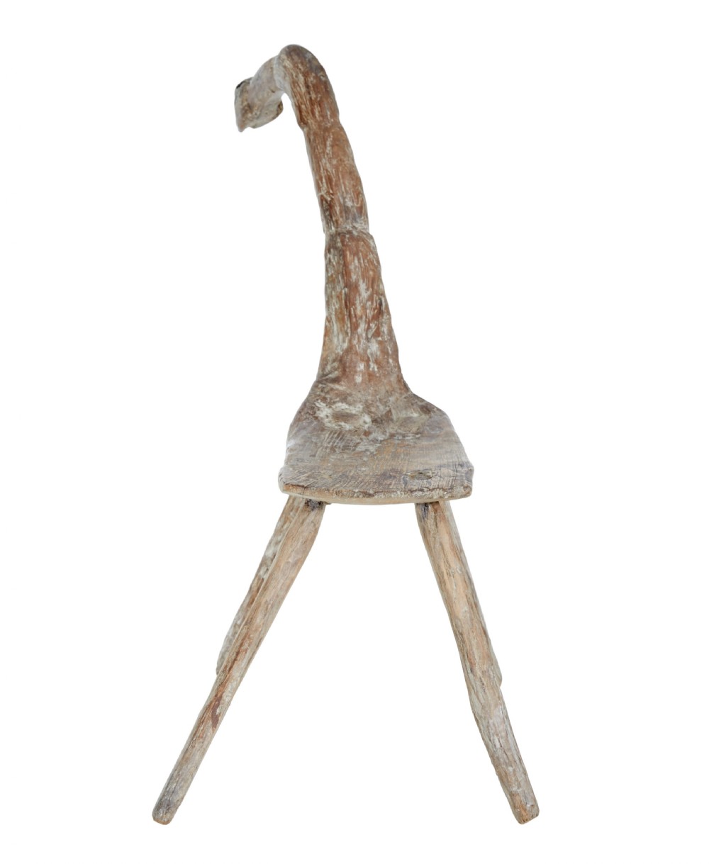 A rustic 19th-century childs stool crafted from weathered natural form oak timber, featuring a curved zoomorphic backrest and four splayed legs. View V