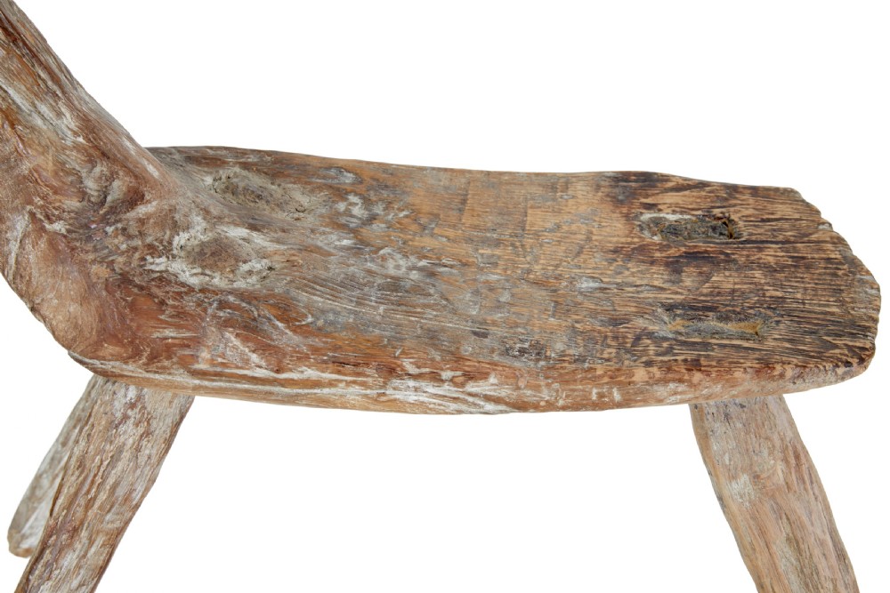 A rustic 19th-century childs stool crafted from weathered natural form oak timber, featuring a curved zoomorphic backrest and four splayed legs. View VI