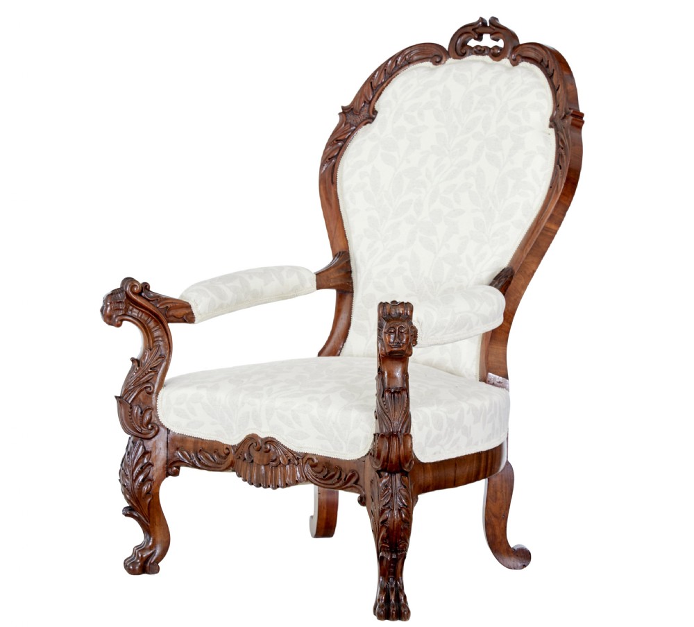 A mid-19th-century carved walnut armchair featuring figurative arm supports and cream patterned upholstery.