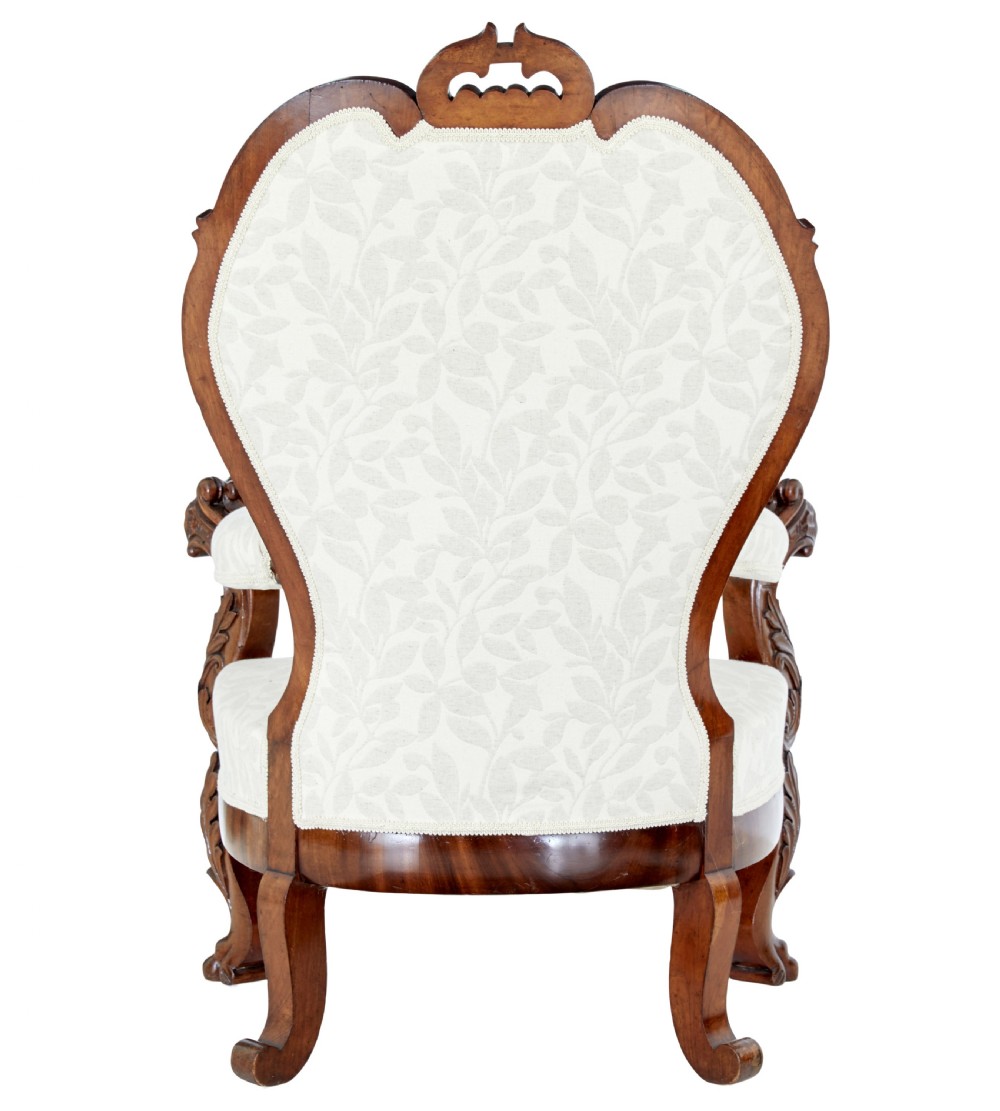 A mid-19th-century carved walnut armchair featuring figurative arm supports and cream patterned upholstery. View V