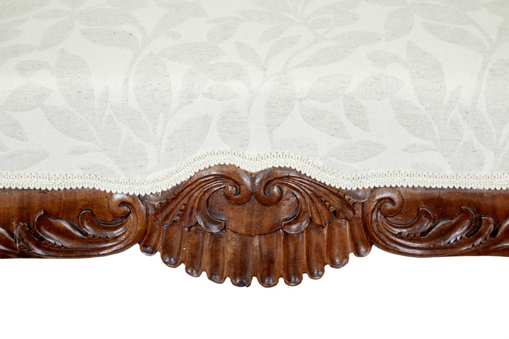 A mid-19th-century carved walnut armchair featuring figurative arm supports and cream patterned upholstery. View X
