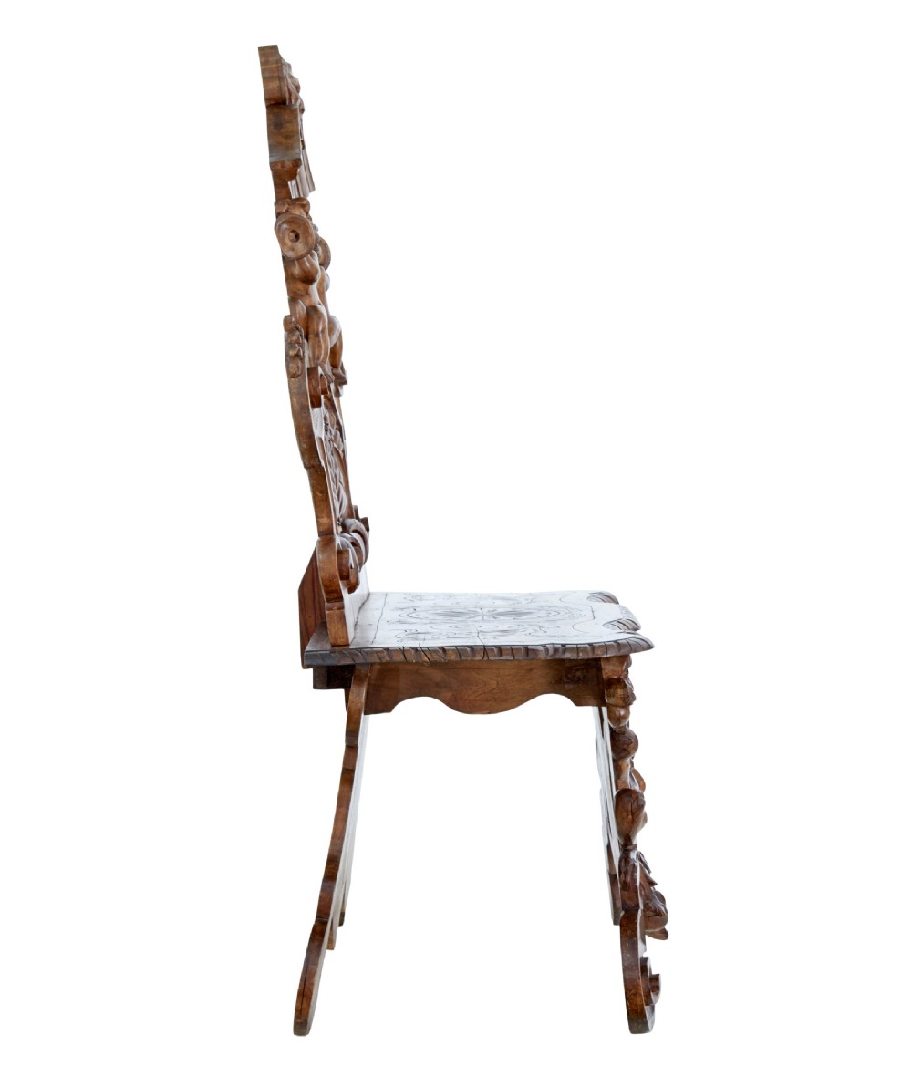 A 19th-century Flemish walnut hall chair decorated with openwork carvings of grotesque masks, cherubs blowing trumpets, and a central shield motif. View V