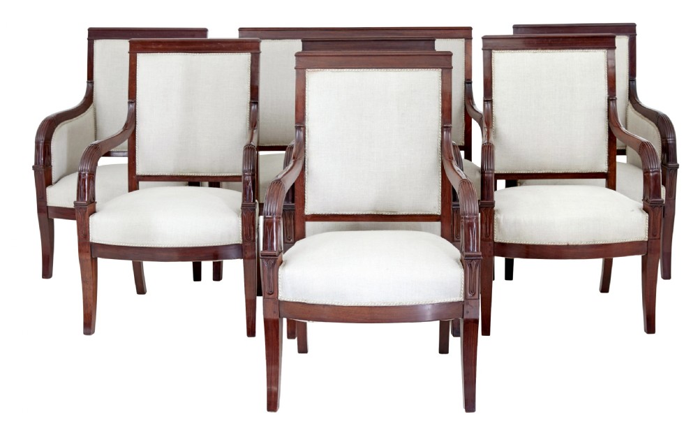 A seven-piece nineteenth-century French Empire mahogany salon suite upholstered in off-white fabric with carved reeded armrests.