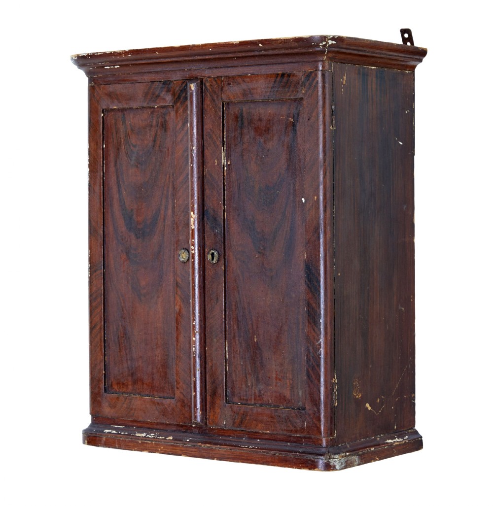 A 19th-century Scandinavian wall cabinet featuring a dark reddish-brown faux-grained paint finish, two panelled doors with brass keyholes, and a moulded top cornice.