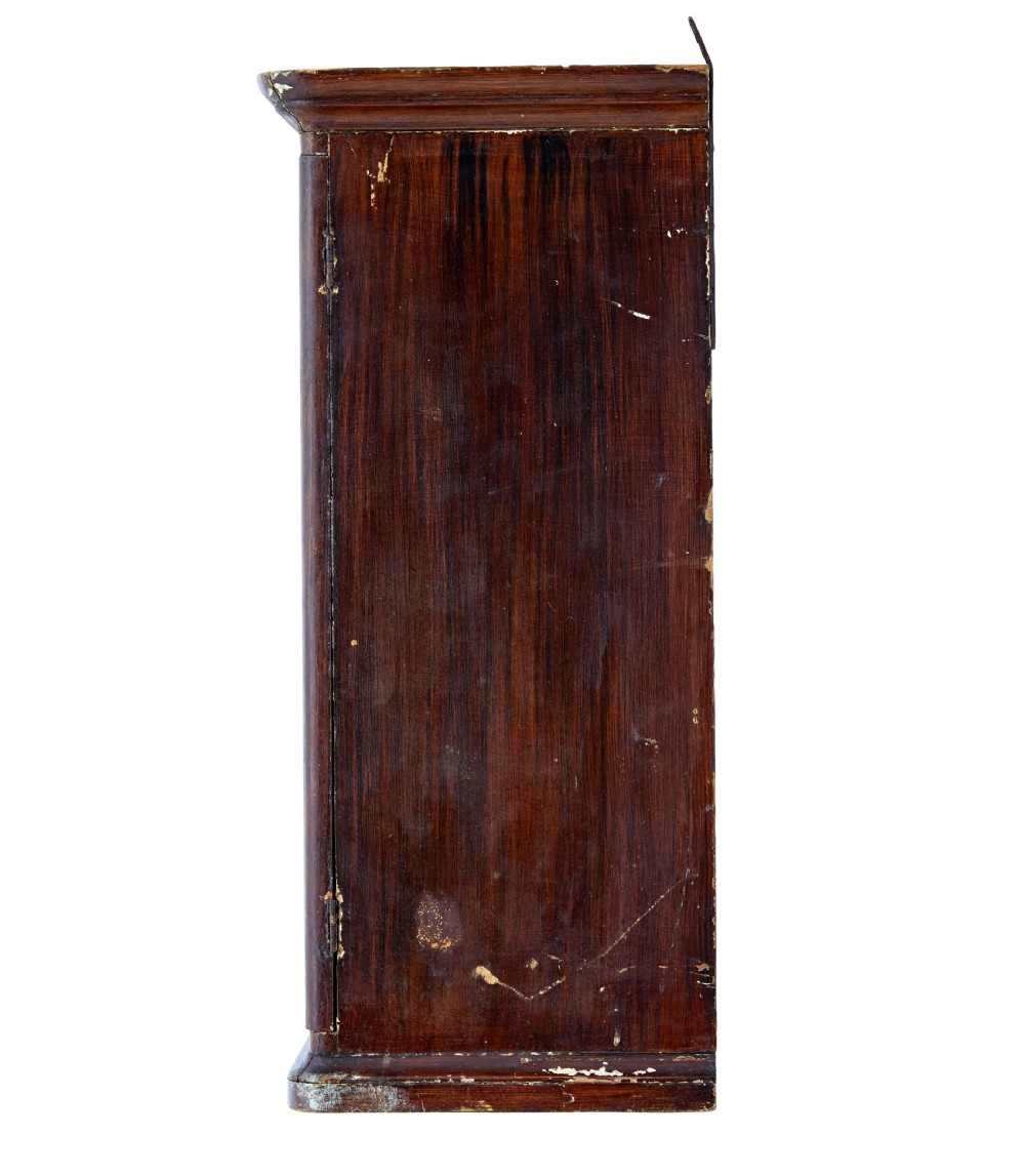 A 19th-century Scandinavian wall cabinet featuring a dark reddish-brown faux-grained paint finish, two panelled doors with brass keyholes, and a moulded top cornice. View V