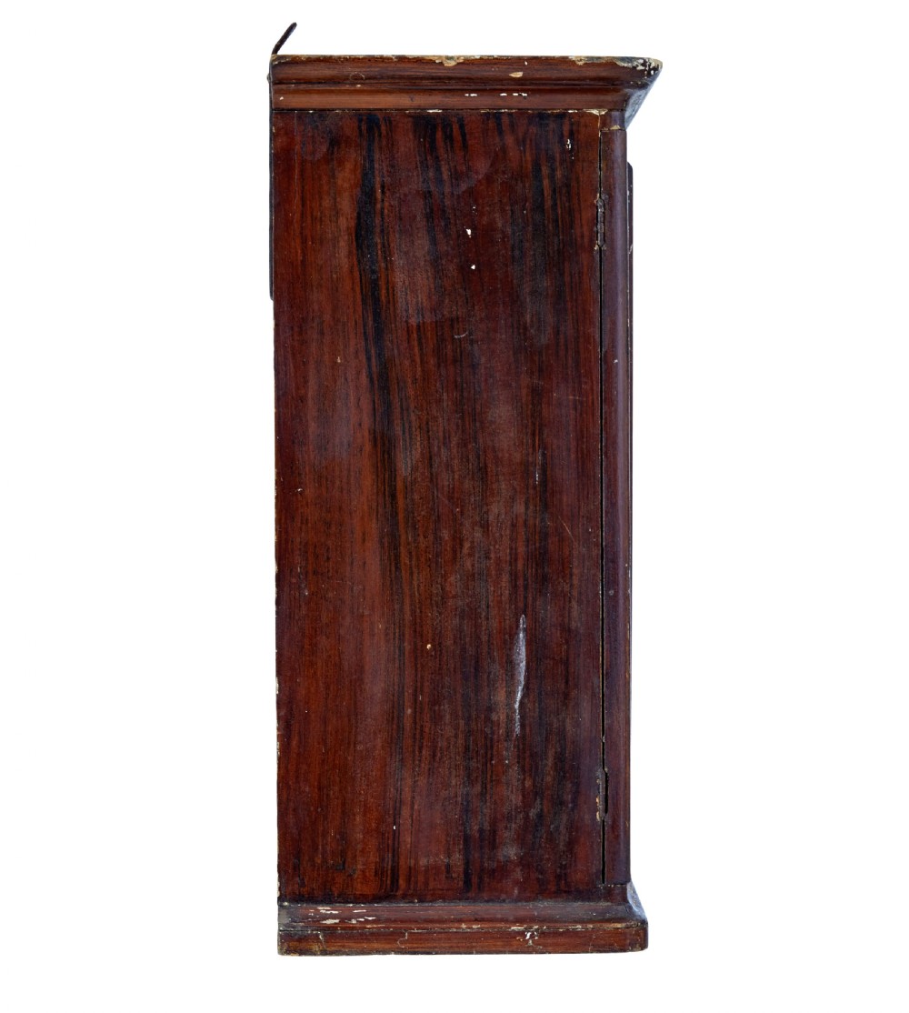 A 19th-century Scandinavian wall cabinet featuring a dark reddish-brown faux-grained paint finish, two panelled doors with brass keyholes, and a moulded top cornice. View VI