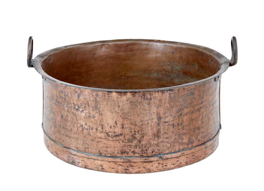 A large round 19th-century hand-hammered copper cooking vessel featuring dual vertical loop handles attached with rivets.