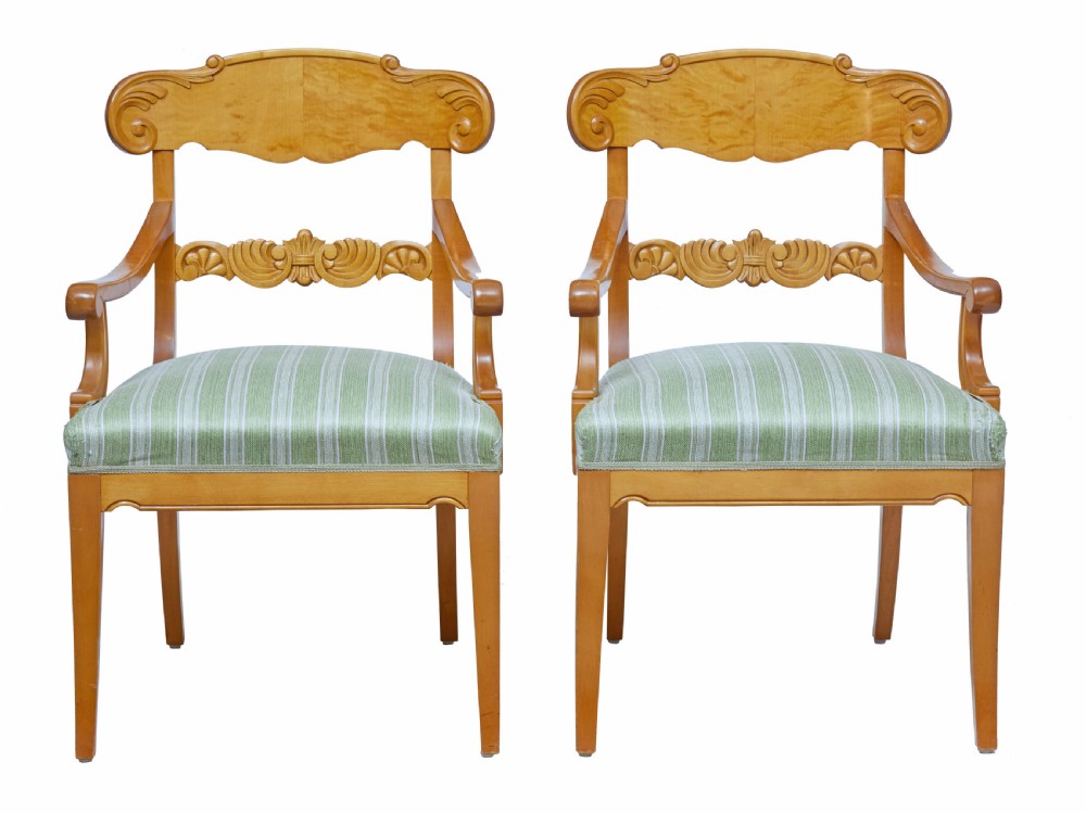 A pair of early 20th-century Swedish birch armchairs featuring carved scroll crests, central relief back rails, and green striped upholstered seats.
