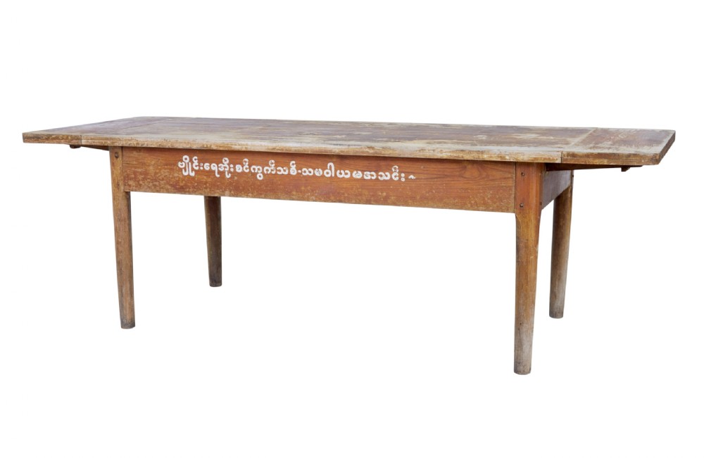 A long 19th-century Burmese teak table with a weathered brown finish and white hand-painted Burmese script across the front frieze.