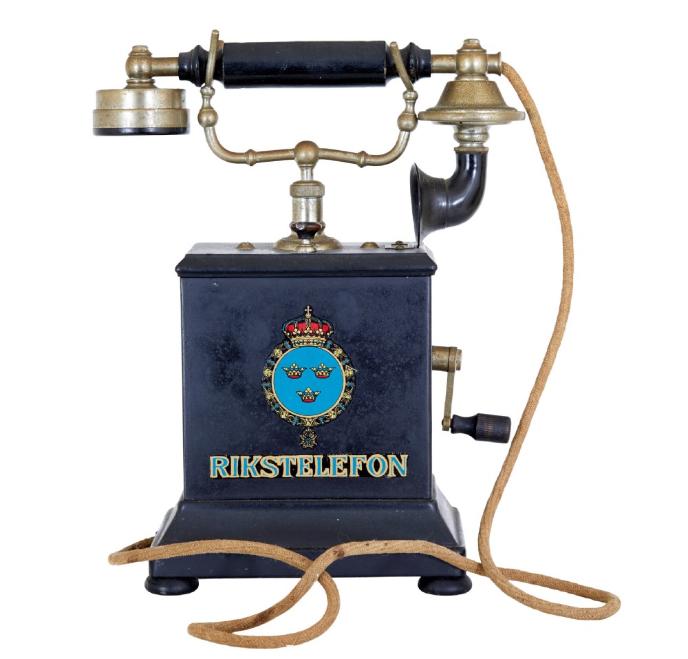 An early twentieth-century black metal Swedish Rikstelefon tabletop telephone with a brass handset cradle, fabric cord, side hand crank, and central blue crown decal.