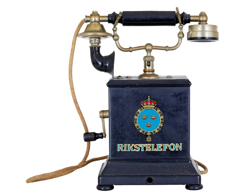 An early twentieth-century black metal Swedish Rikstelefon tabletop telephone with a brass handset cradle, fabric cord, side hand crank, and central blue crown decal. View IV