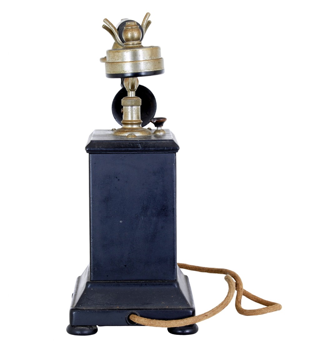 An early twentieth-century black metal Swedish Rikstelefon tabletop telephone with a brass handset cradle, fabric cord, side hand crank, and central blue crown decal. View V