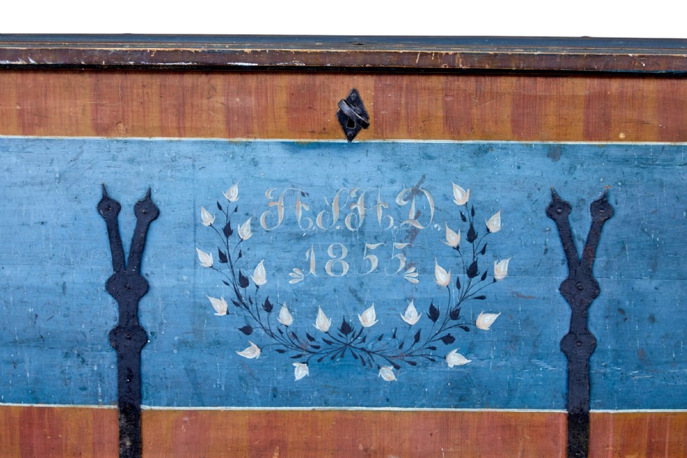 A mid-19th-century Swedish painted wooden coffer featuring blue centre panels decorated with a floral wreath and the date 1855, framed by terracotta borders and black wrought iron straps. View VI